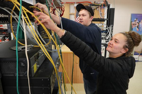 Man and a woman plugging in cables into a network switch